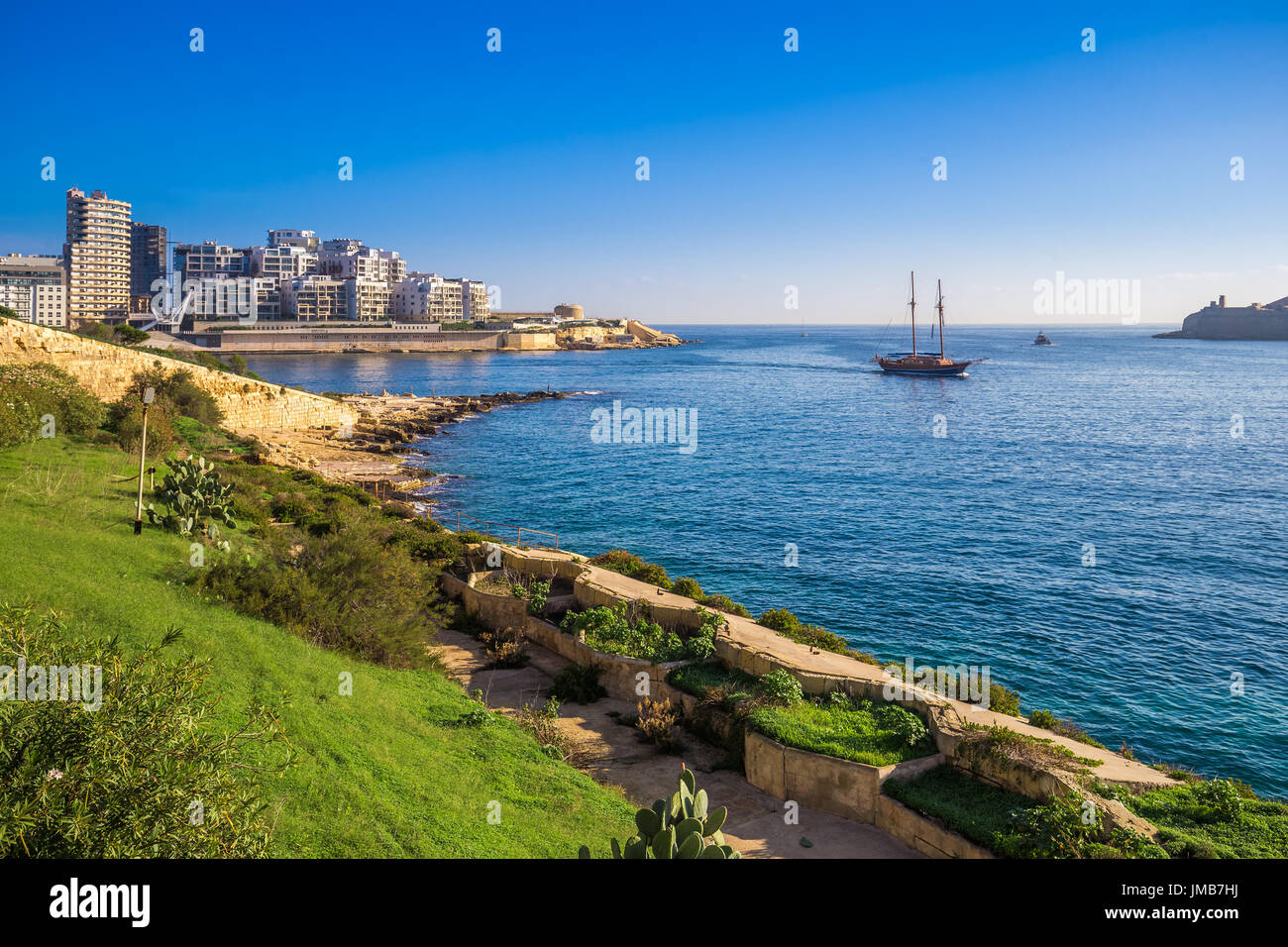 Valletta, Malta - Skyline view of Sliema at sunrise shot from Manoel island at spring time with sailing boat, blue sky and green grass Stock Photo
