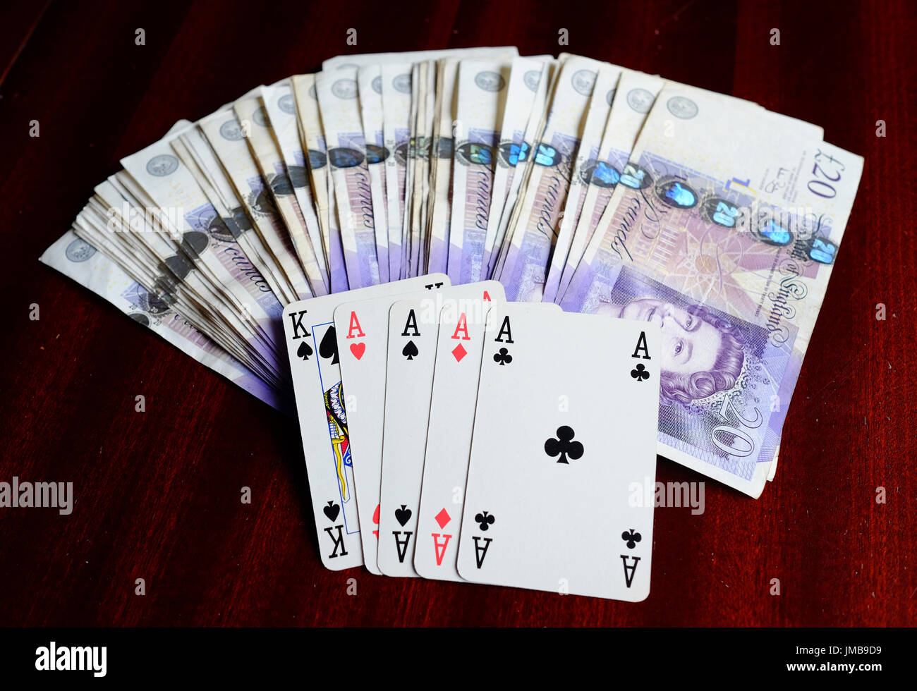 Four aces and a king, a lucky winning poker hand and a fortune in £20 notes on a dark table Stock Photo