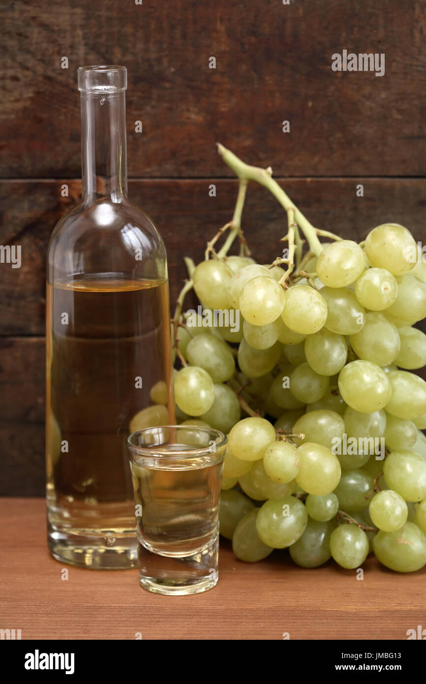 Open bottle of grappa near wineglass and bunch of grapes against old wooden background Stock Photo