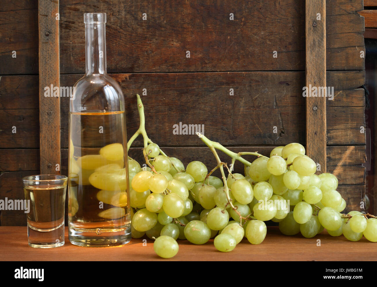 Glass full of grape Italian vodka “grappa” near bottle and bunch of grapes on old wooden background Stock Photo