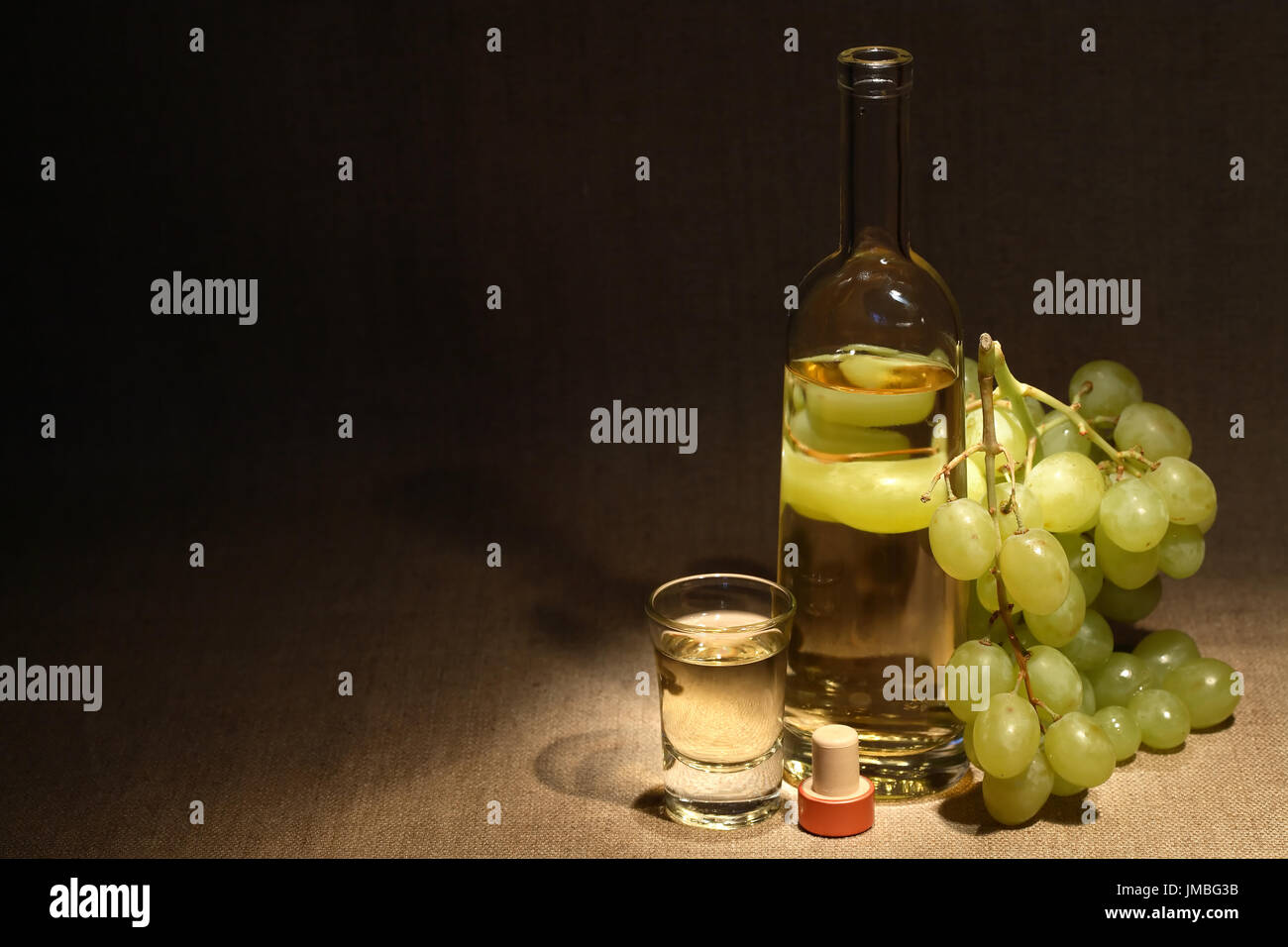 Glass full of grape Italian vodka «grappa» near bottle and bunch of grapes on old canvas background Stock Photo