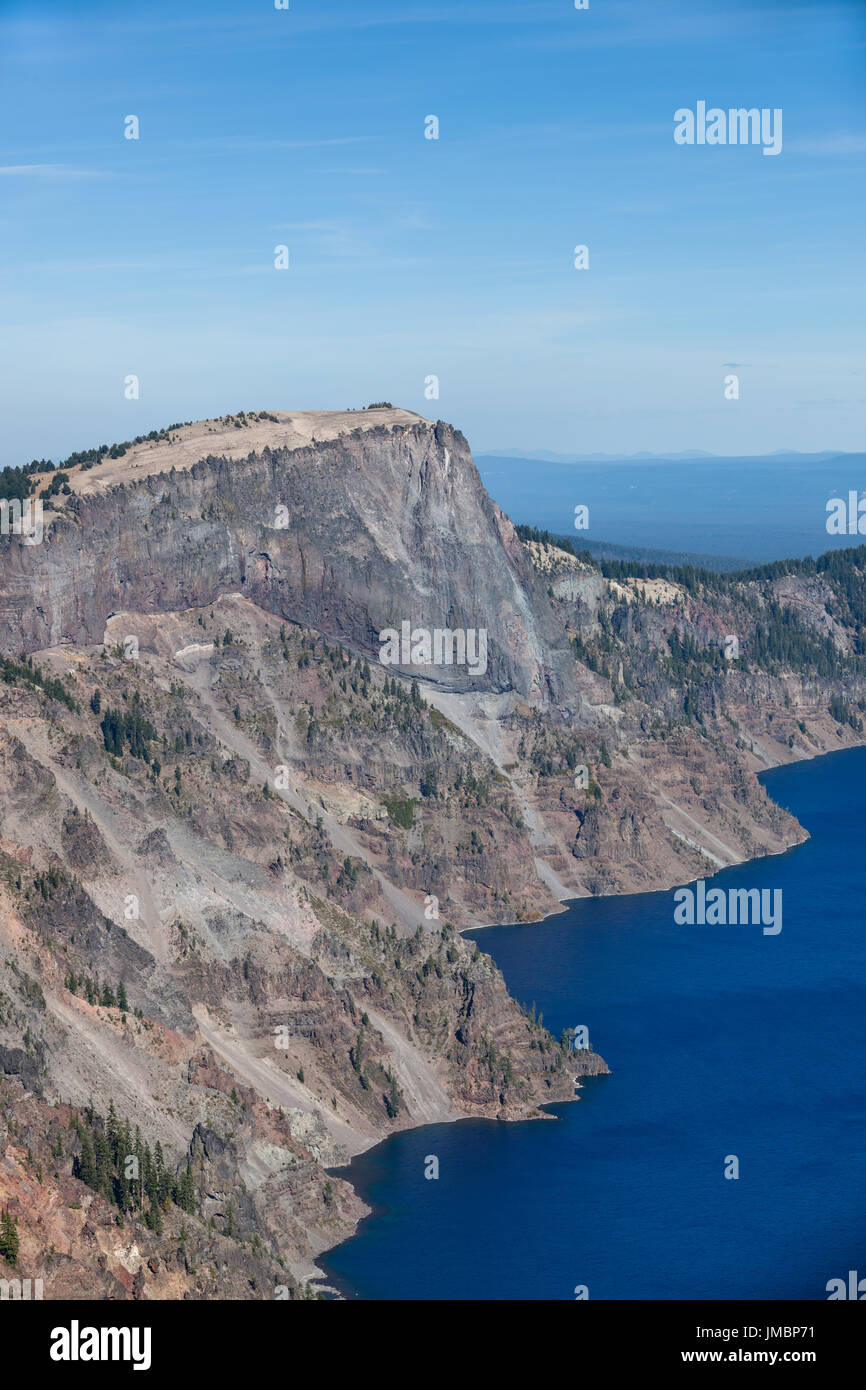 Large volcanic rock of Llao Peak at Crater Lake National Park steeply dropping almost two thousand feet to the surface of the blue lake. Stock Photo