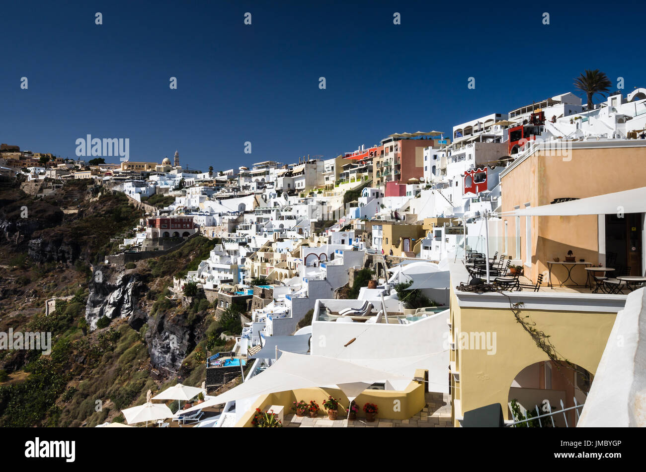 Fira, Thira town, Santorini Cyclade islands, Greece. Beautiful view of the town with white buildings, blue church's roofs and many colored flowers. Stock Photo