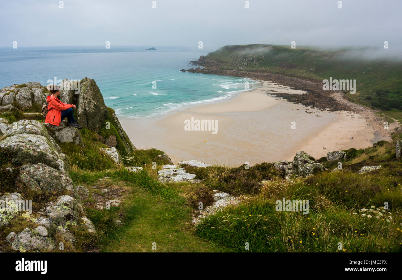 Young woman sitting by herself looking out at empty cove Gwynver Beach, Cornwall, England, UK Stock Photo