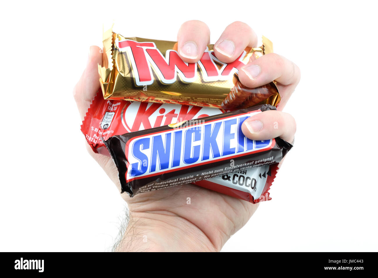A hand grabs KitKat, Snickers and Twix chocolate bars isolated on white