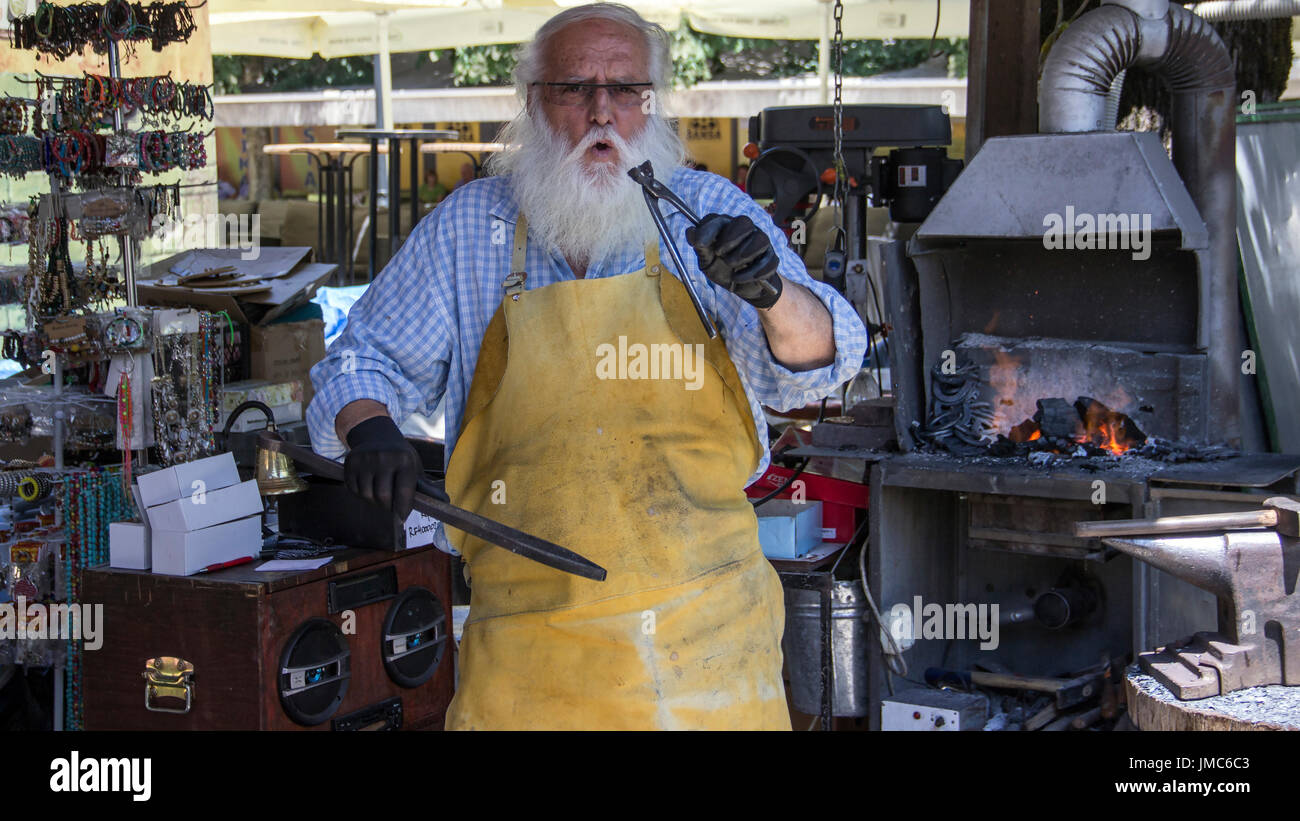 Cetinje, Montenegro - Aged blacksmith making horseshoe souvenirs and entertaining tourists in a street workshop Stock Photo