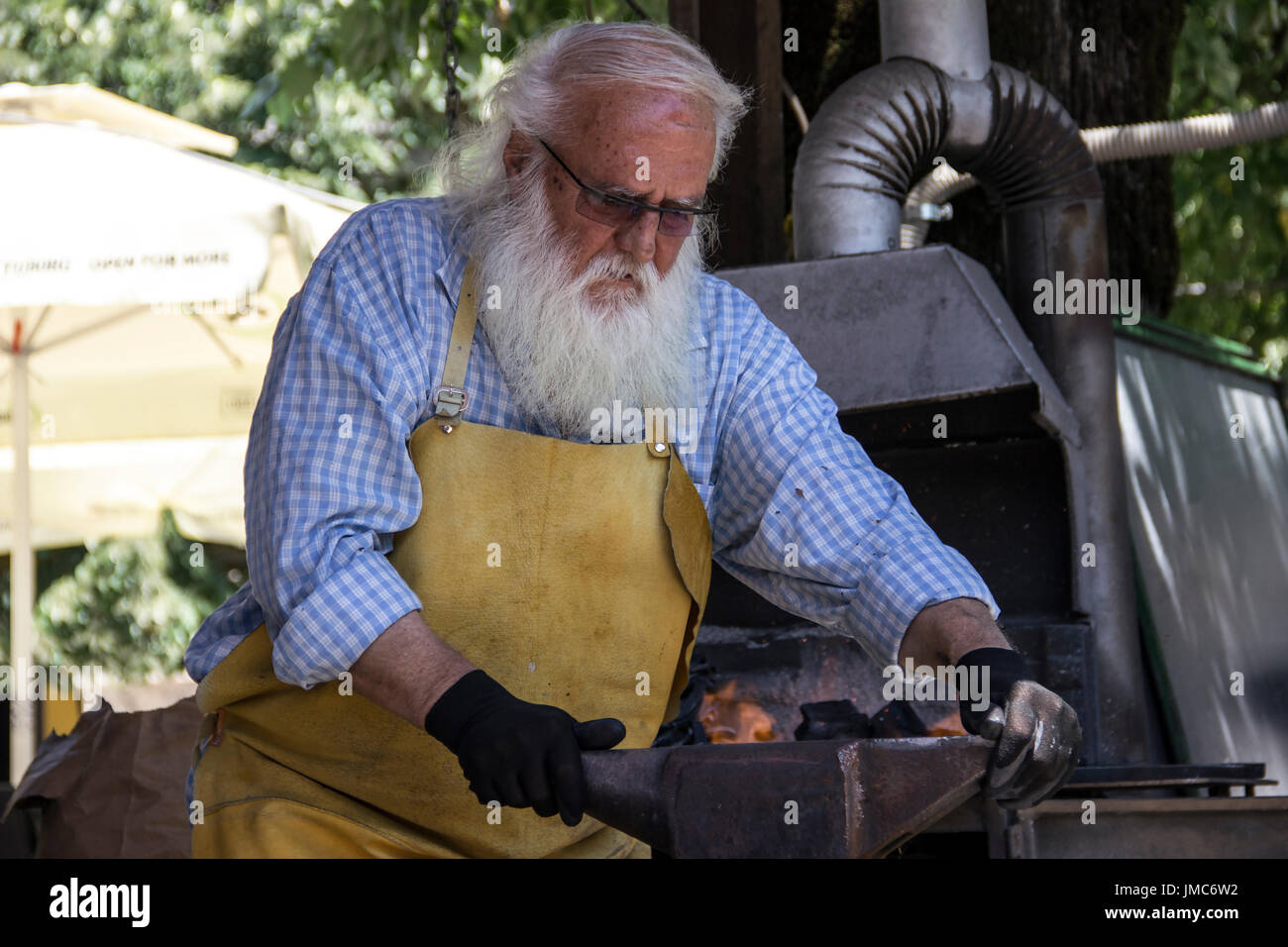 Cetinje, Montenegro - Aged blacksmith making horseshoe souvenirs and entertaining tourists in a street workshop Stock Photo