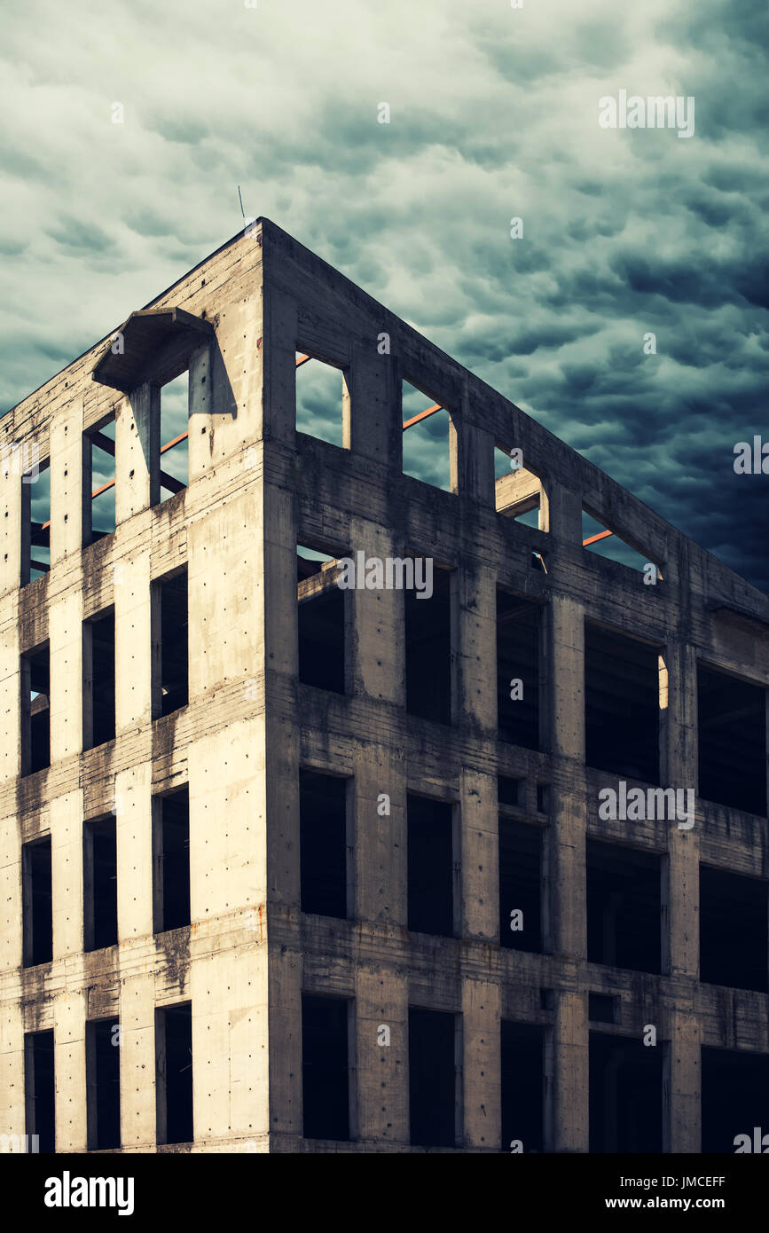 Unfinished abandoned concrete building facade with dark stormy clouds in the background Stock Photo