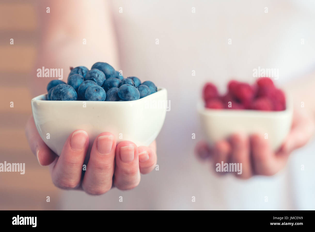 Choose blueberries over raspberries, female hands with berry fruit, selective focus Stock Photo