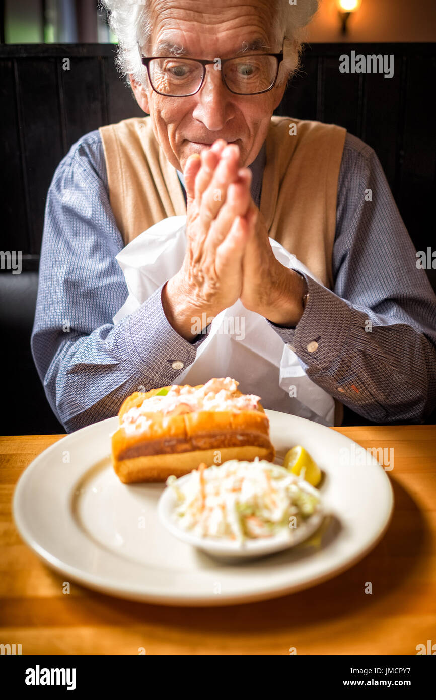 Old man rubs his hands in anticipation of eating his favorite food in a restaurant. Lobster roll in Maine coast. Stock Photo