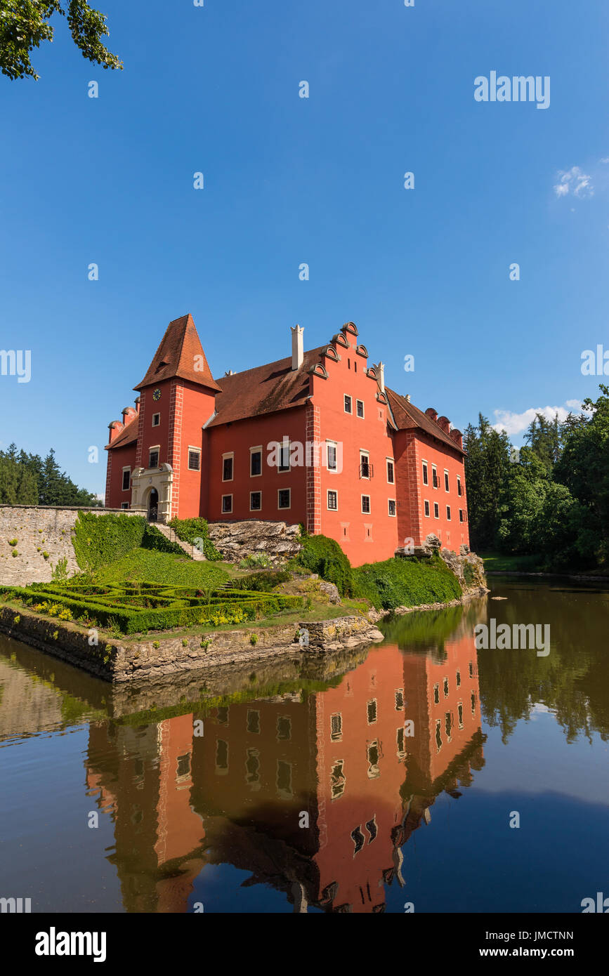 Vertical photo of nice romantic castle. The bulding has red color and is build on small lake where is visible the reflection of castle. The bridge, sm Stock Photo