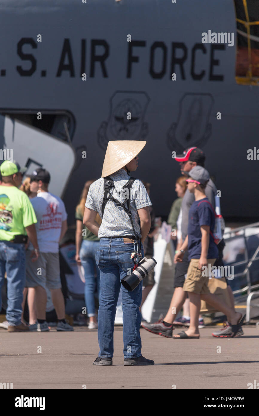 Guy wearing straw conical asian style hat taking photos at airshow. Stock Photo