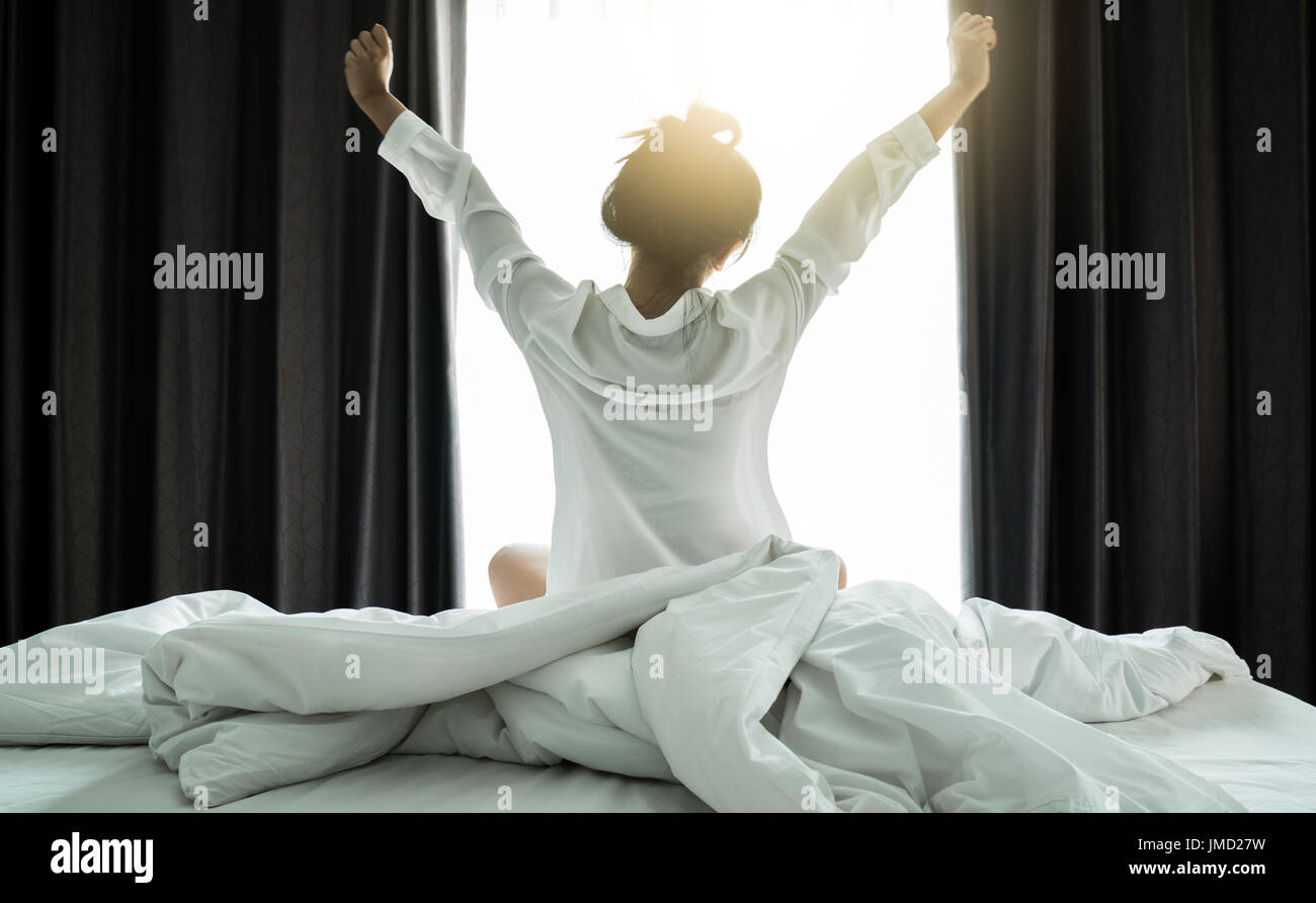 Asian women wake up from sleep. are  stretch herself  in the morning on the weekend sit on the bed at luxury room in Relax and weekend concept Stock Photo