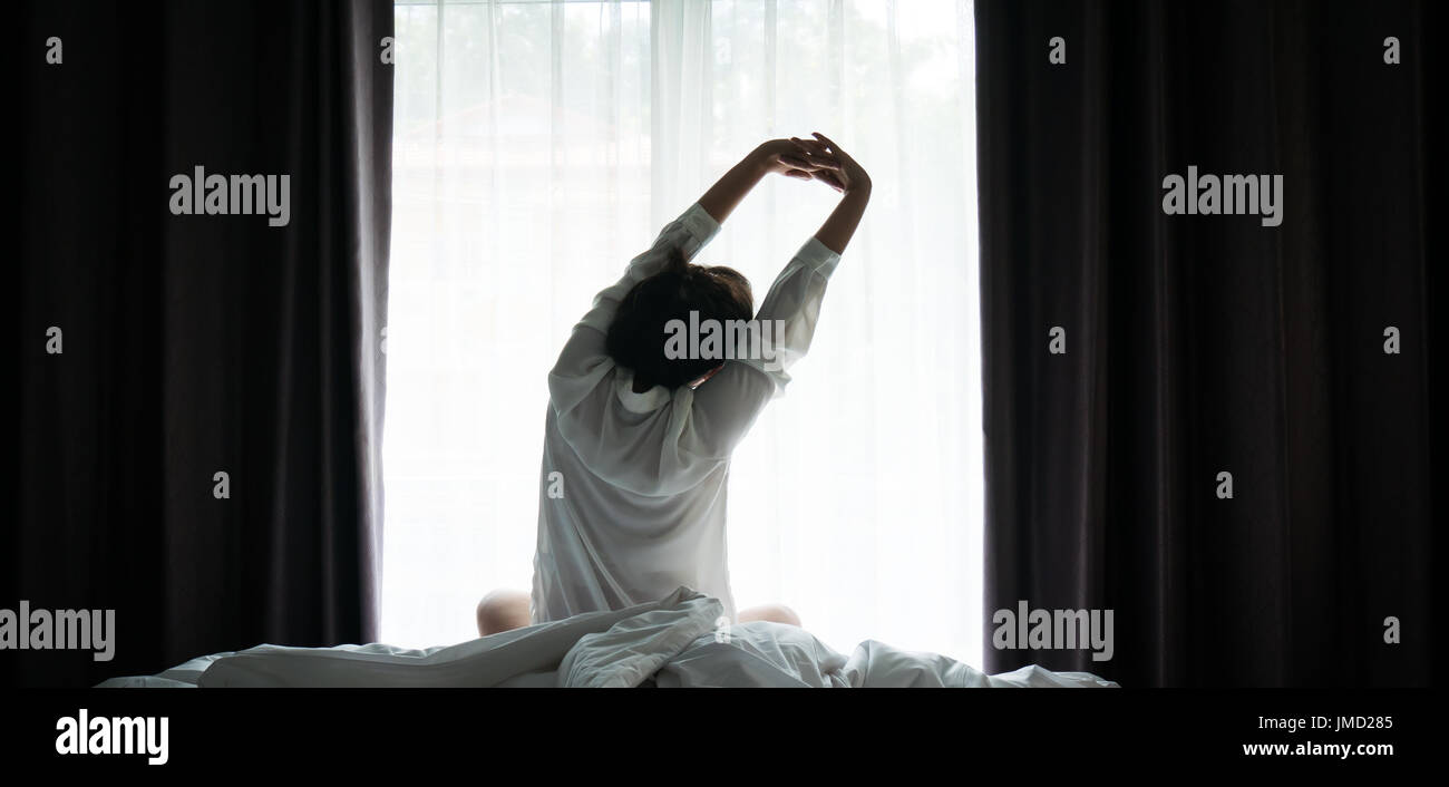 Asian women wake up from sleep. are  stretch herself  in the morning on the weekend sit on the bed at luxury room in Relax and weekend concept Stock Photo
