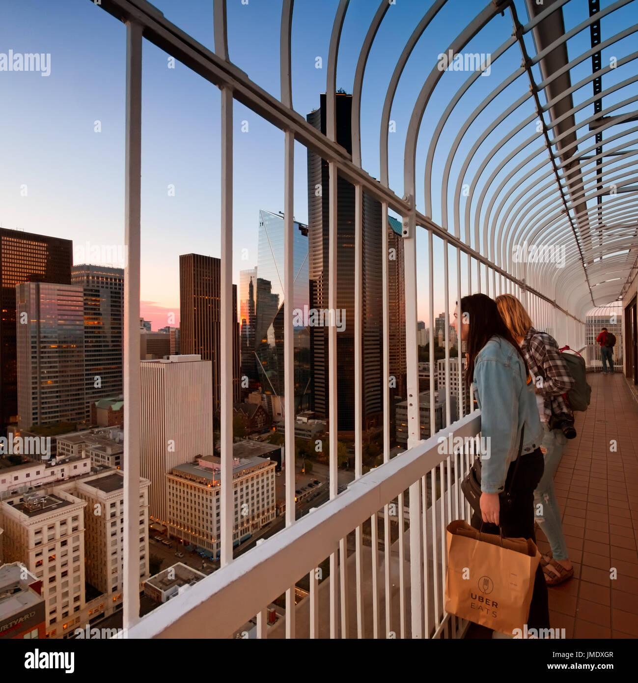 SEATTLE - July 16, 2017: Two young women stare at beautiful aerial view of downtown Seattle at sunset from a skyscraper viewing deck. One holds a pape Stock Photo