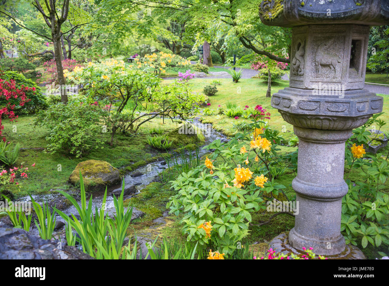 Stone Lantern near Meandering Stream in Flowering Japanese Garden Stock Photo