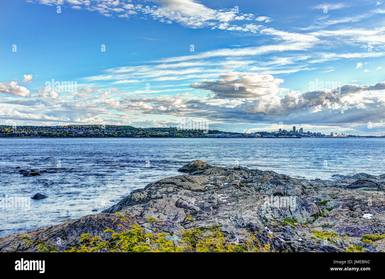 Landscape view of Saint Lawrence river from Ile D'Orleans, Quebec, Canada in summer with green plants, rocks and cityscape skyline of city and Levis t Stock Photo