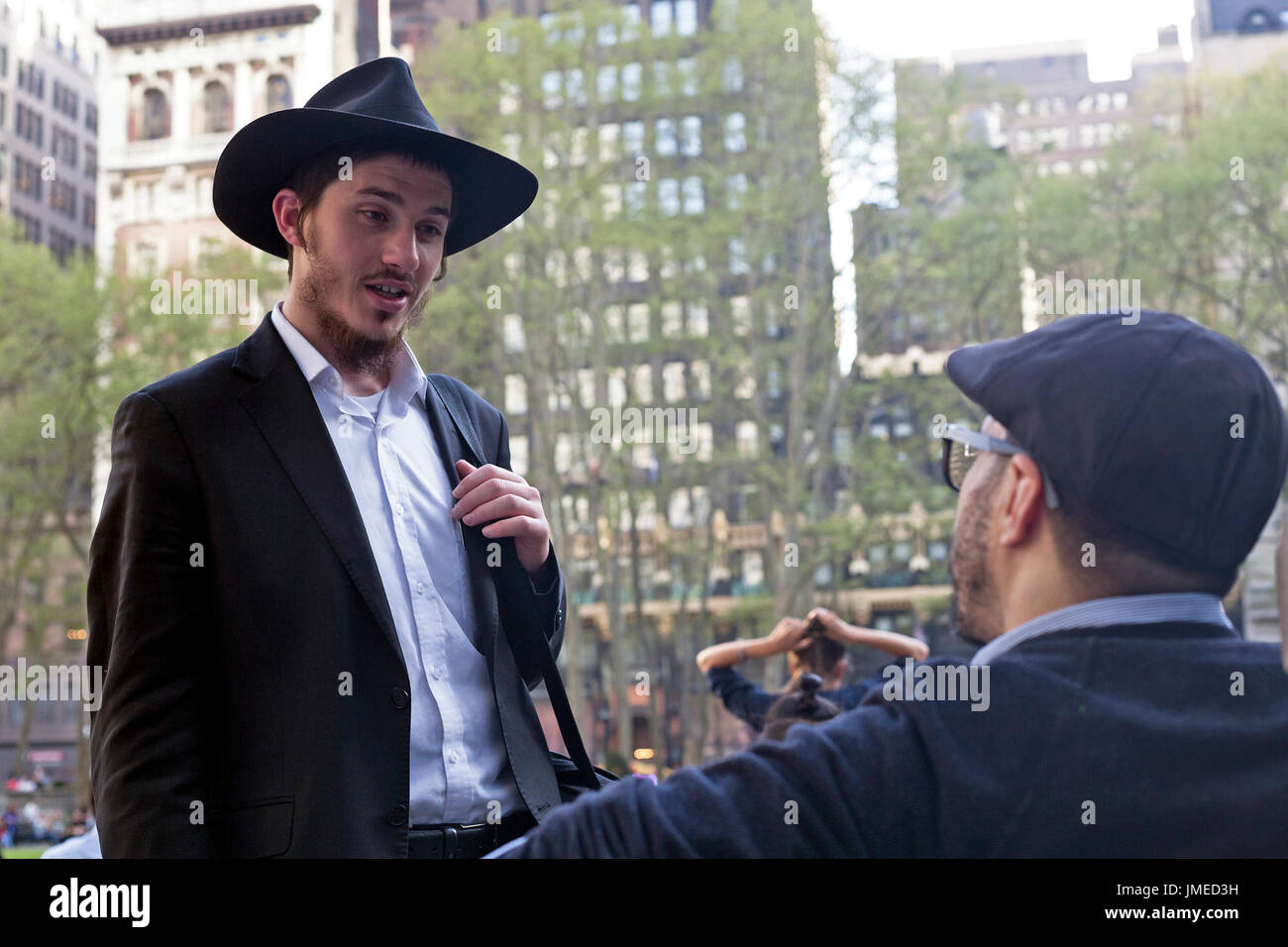 A young Orthodox Jewish man speaks to someone in Bryant Park in New York City. Stock Photo