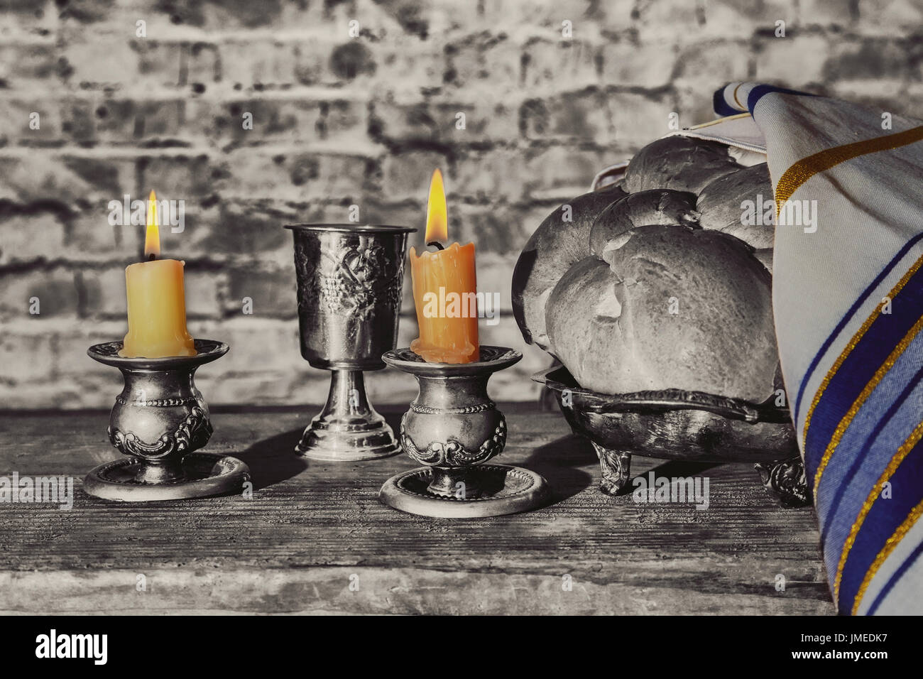 Silver kiddush cup, crystal candlesticks with lit candles, and challah