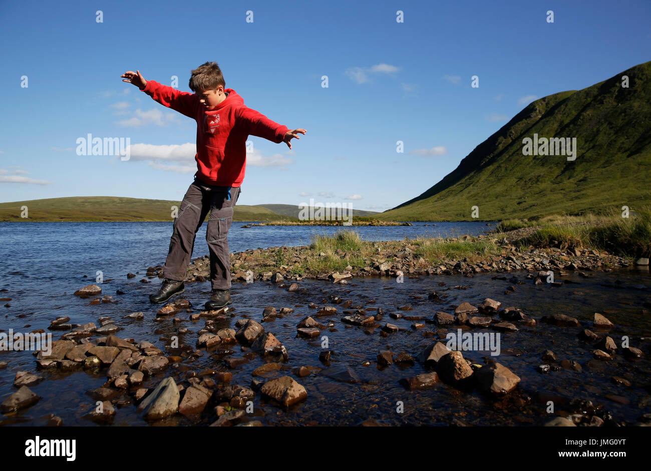 A teenage boy walks on stepping stones to cross a stream at Loch Skeen and Grey Mare's Tail in the Moffat Hills, Dumfries and Galloway, Scotland, UK Stock Photo