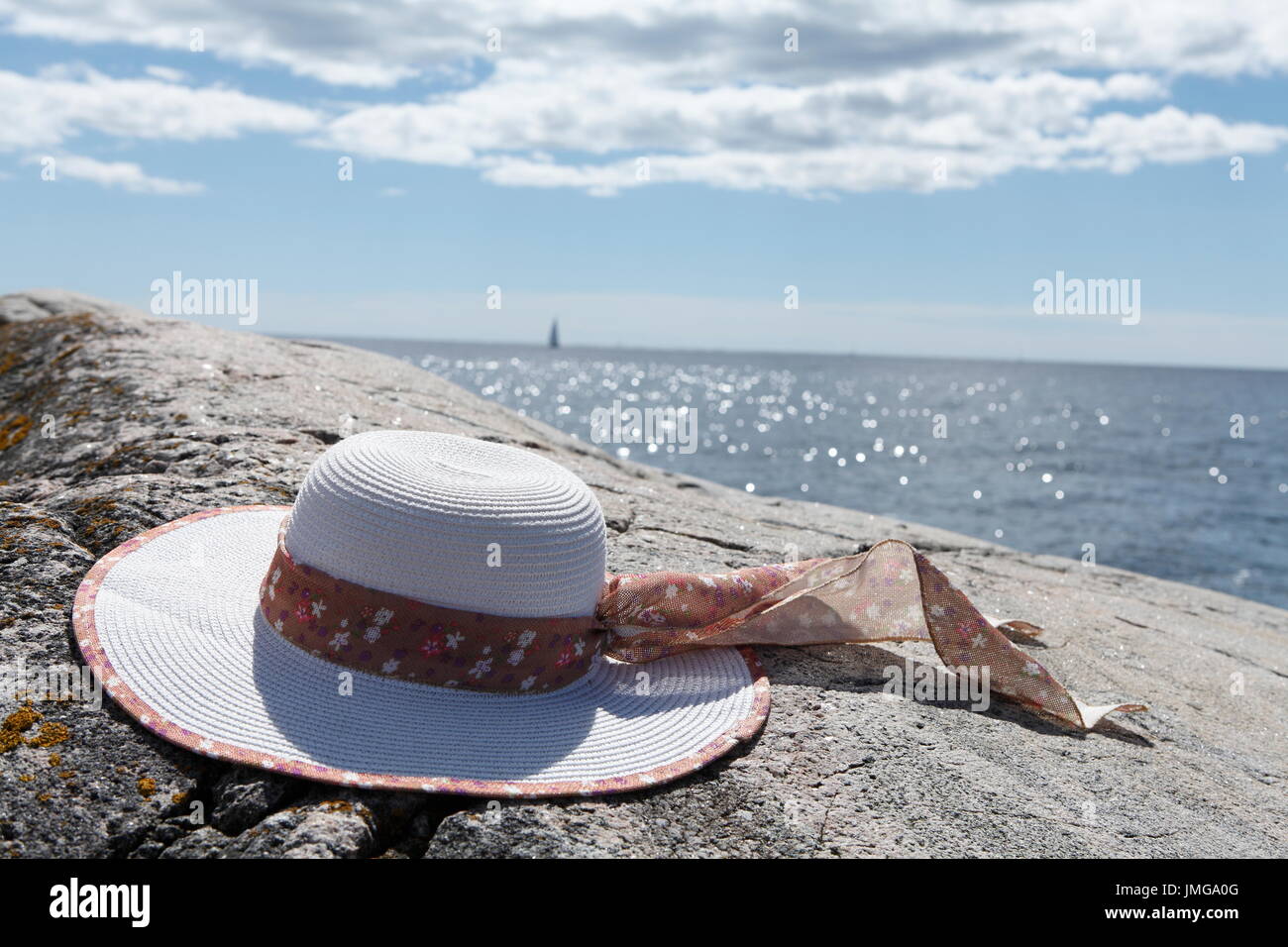 Relaxing in the summer sun with the ocean in the background. Sails in the horizon. Summer hat close by. Stock Photo