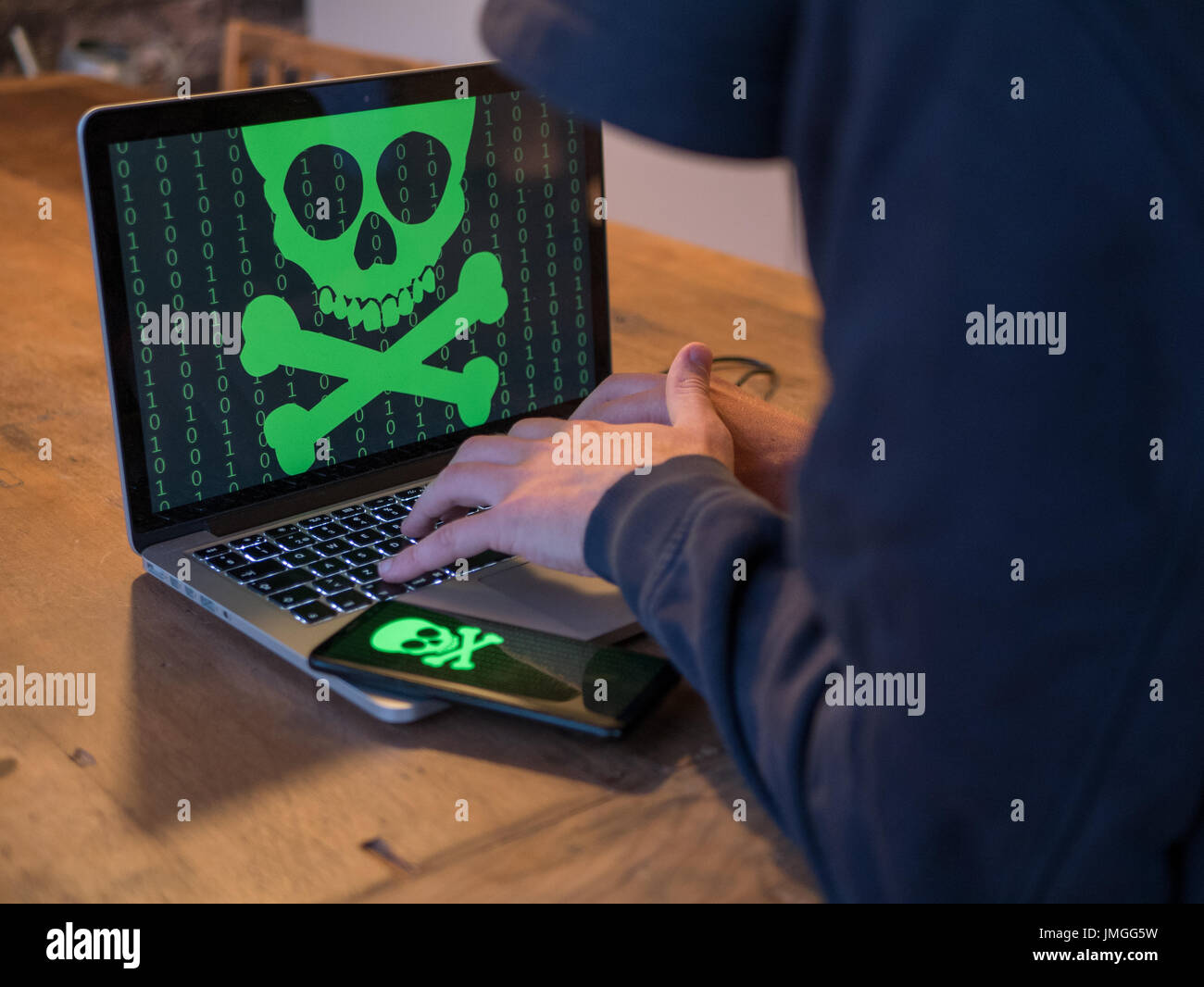 Hacker in hoodie is using a computer. Mobile is also infected. Stock Photo