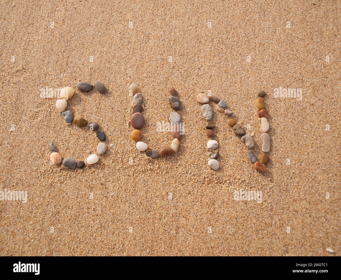word sun written with stones and shells on the beach by the ocean Stock Photo
