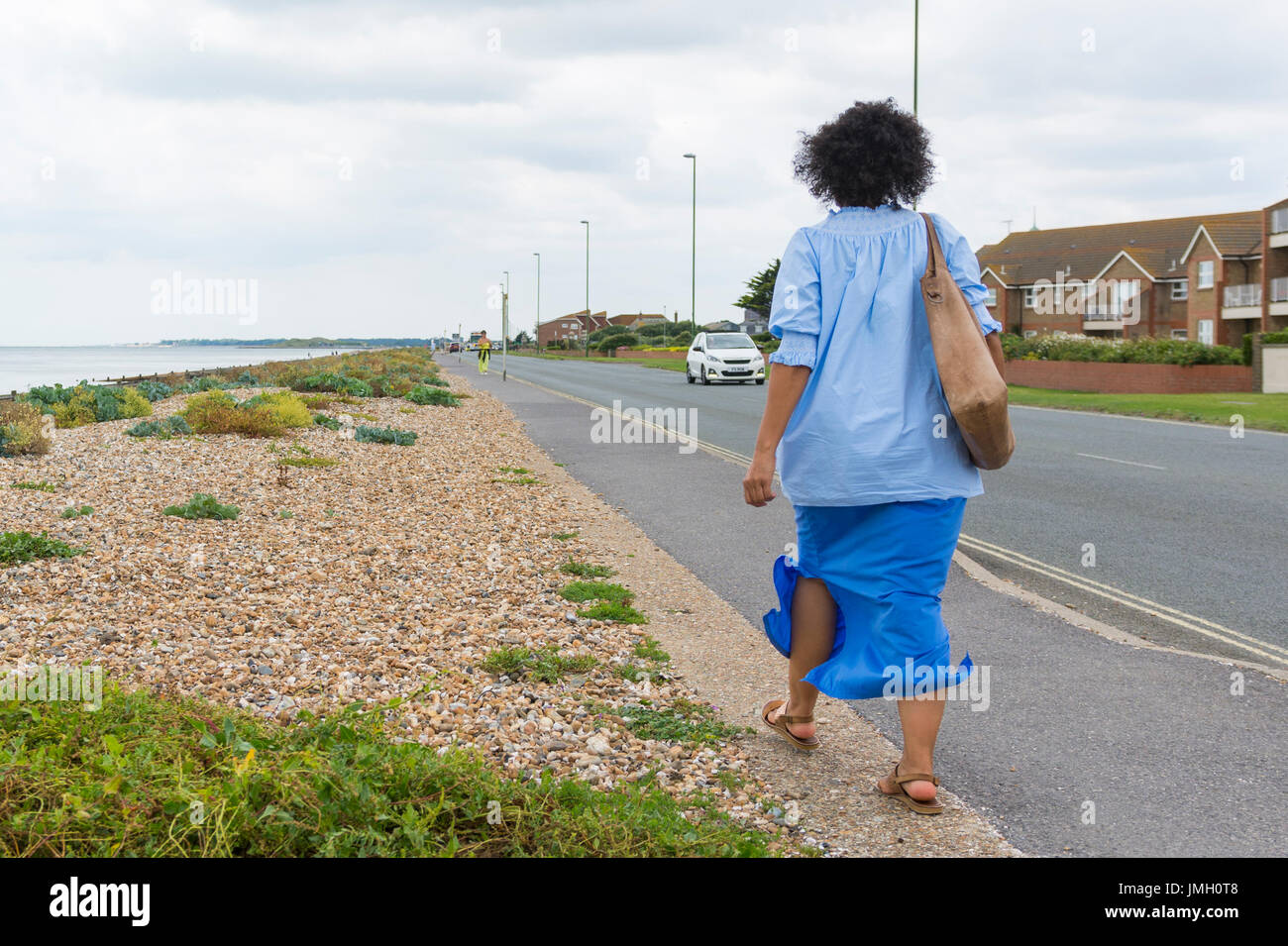 Woman walking along a seafront road by a beach on a windy day. Stock Photo