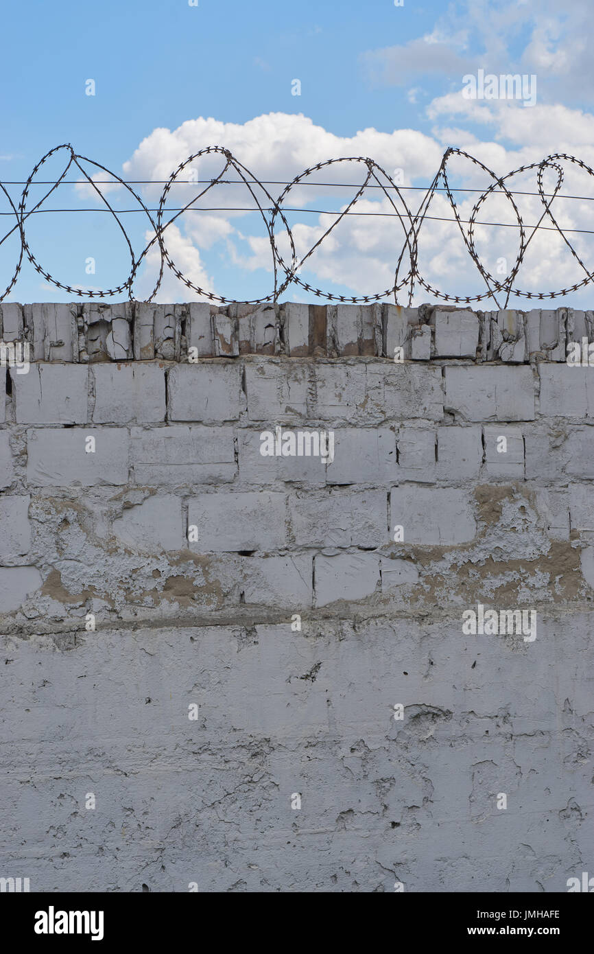 white brick wall with razor barbed wire with blue sky and clouds behind ...