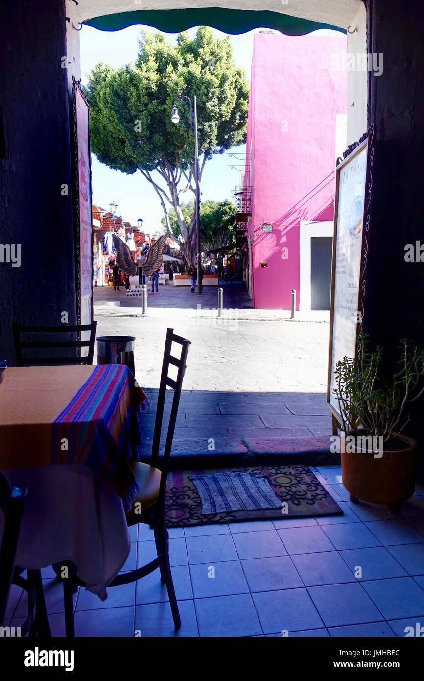 Looking out empty, cool interior, of Mexican cafe door onto pedestrian plaza. Puebla, Mexico. Stock Photo