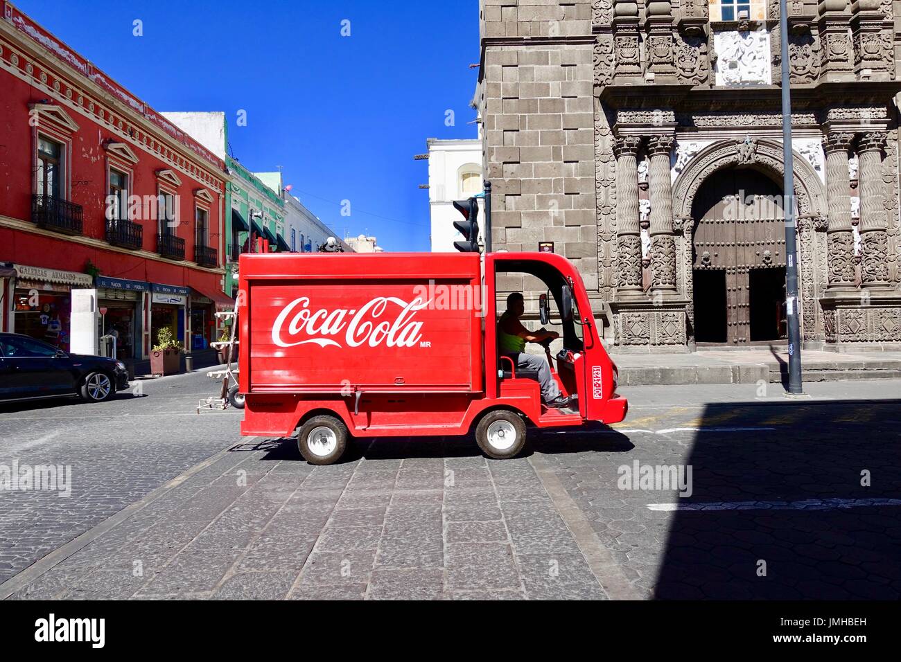 Side view of small-sized, Coca Cola delivery truck passing church on empty, morning streets of Puebla, Mexico. Stock Photo