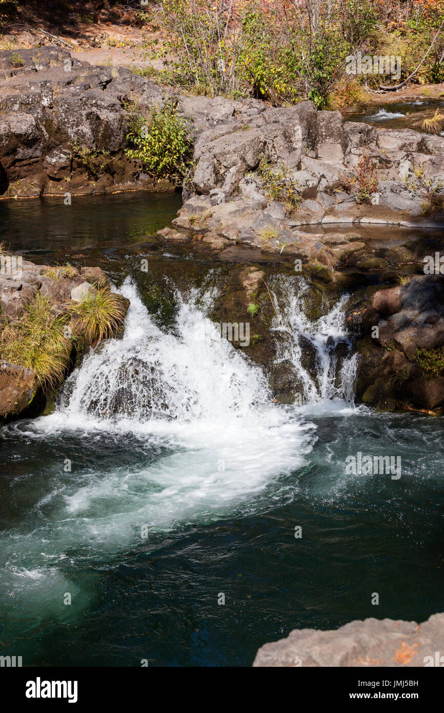 Clean water from a creek flows quickly over an embankment of rocks into a larger pool of