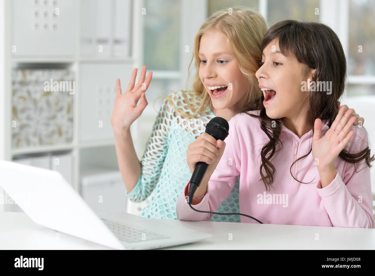 Two teen girls sitting at table and singing karaoke Stock Photo