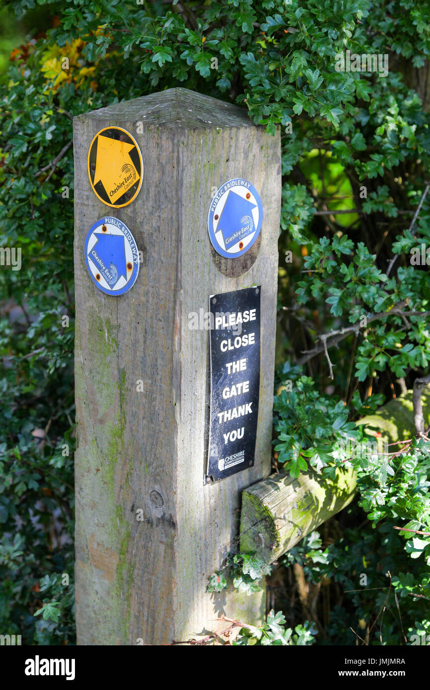 A wooden way marker with yellow arrow footpath sign and saying 'public bridleway' and 'please close the gate' Cheshire East Council Stock Photo