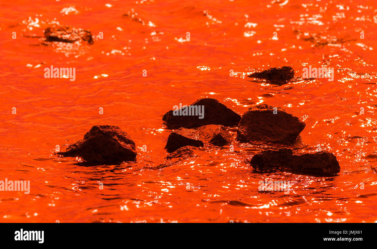 black stones in deep orange water; reflections on the water Stock Photo