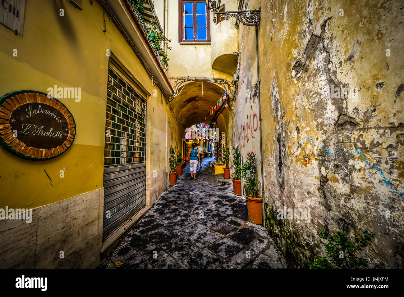 A woman traveling alone walks down a narrow path through a small tunnel in the Mediterranean city of Sorrento Italy Stock Photo