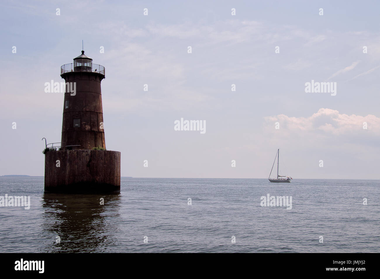 lighthouse with sailboat in the background Stock Photo
