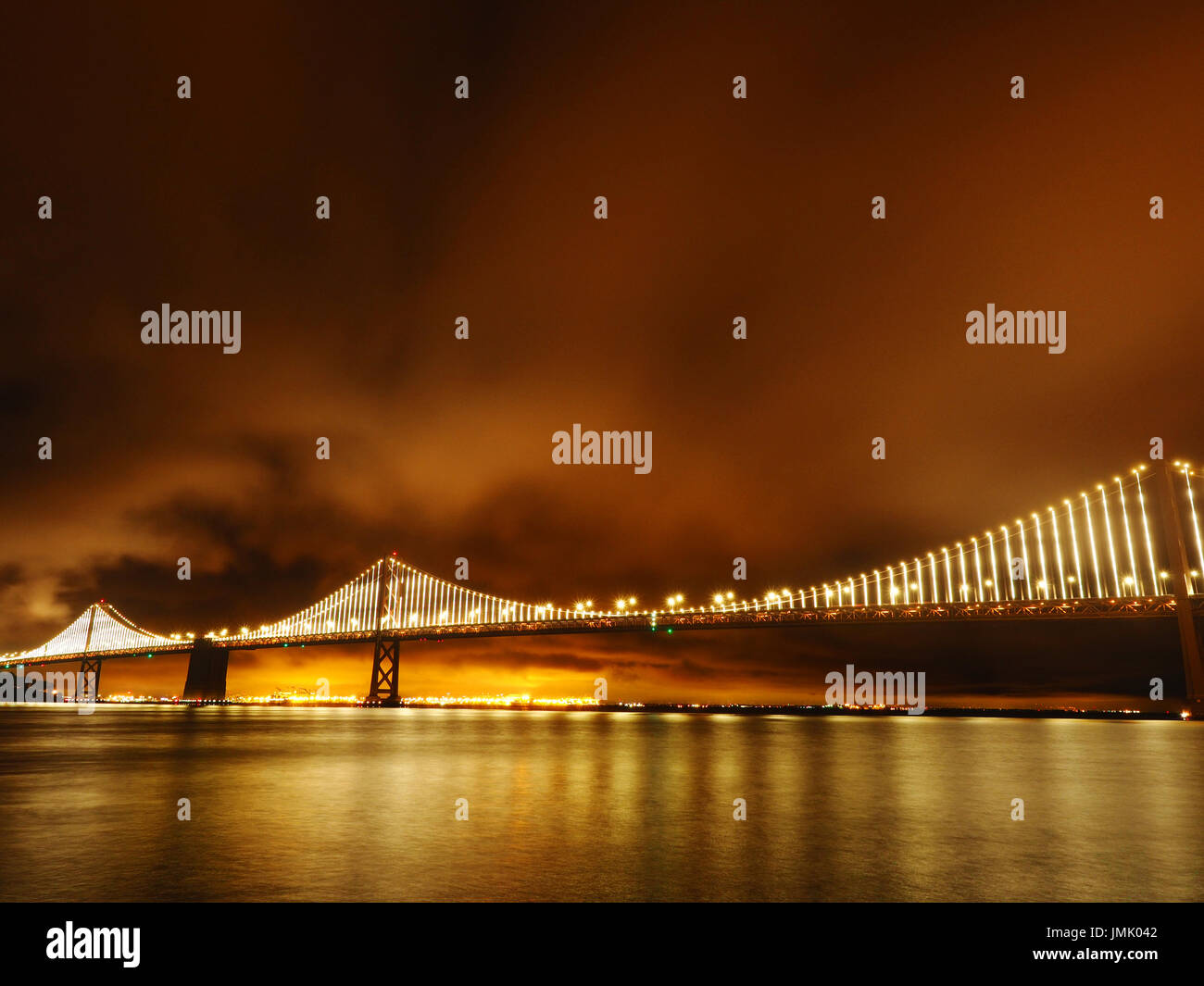 New Bay Bridge at Night as Seen from the Embarcadero with Lights Reflected off of the Bay and Illuminated Clouds, San Francisco, California, USA Stock Photo