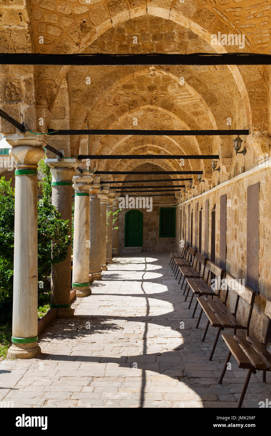 Columned portico with Stone Pillars and  wooden Benches in Mosque in Acri Akko Israel Stock Photo