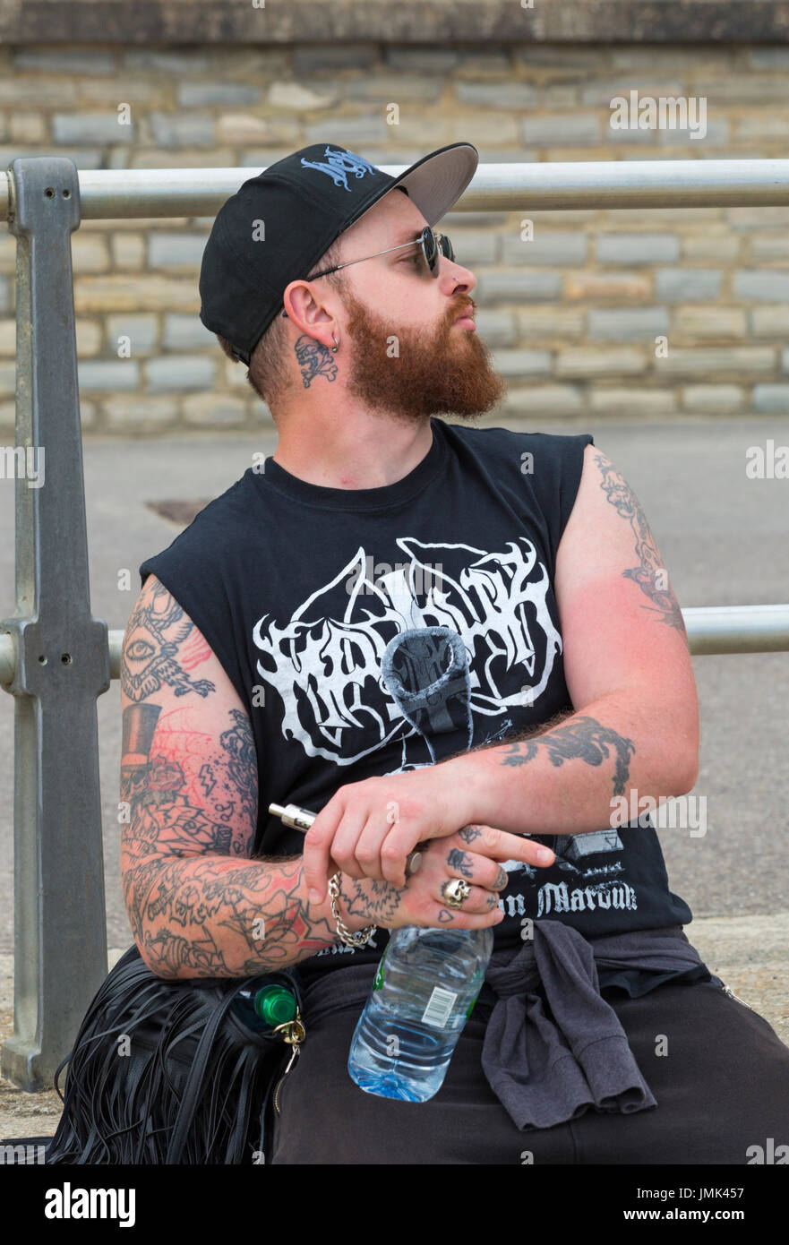 Tattooed man sitting on wall of promenade at Lyme Regis, Dorset in July Stock Photo