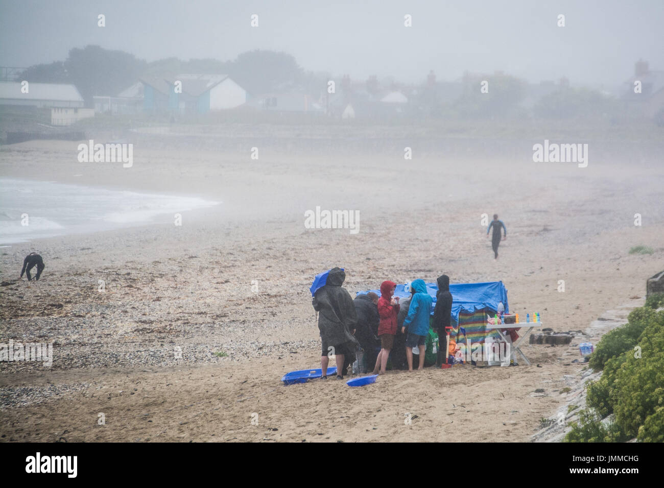 Marazion, Cornwall, UK. 28th July 2017. UK Weather. It was a wet and windy day at Marazion today. This family were determined to make the most of their holiday to Cornwall, even if that meant having the picnic on the beach, in the rain. Credit: cwallpix/Alamy Live News Stock Photo