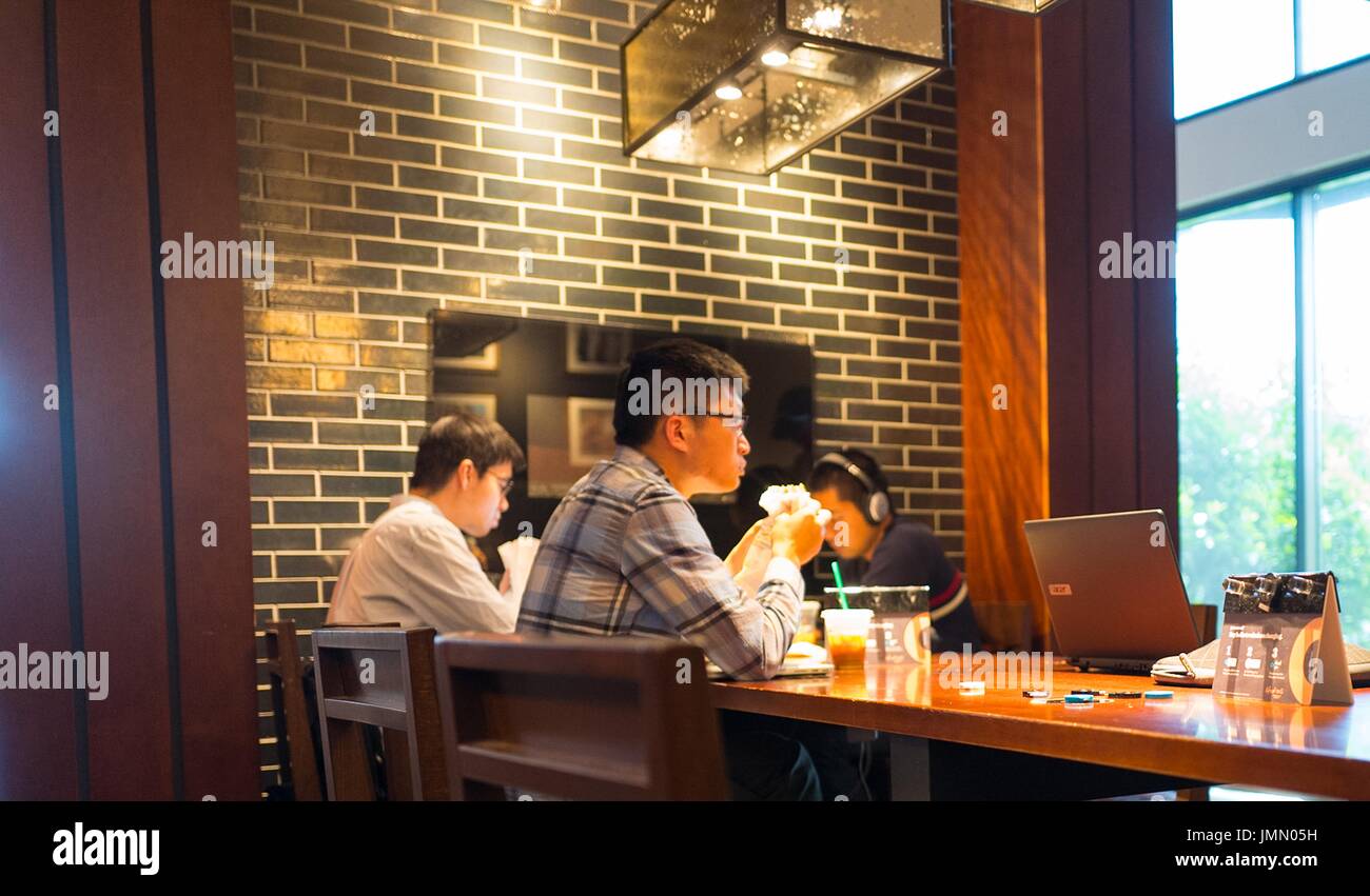People wearing headphones and using laptops gather at a communal table inside a Starbucks cafe in the Silicon Valley town of Mountain View, California, June 4, 2016. With an extremely expensive commercial real estate market in the Valley, it is common for startup founders and other technology workers to work out of cafes and other public spaces. Stock Photo