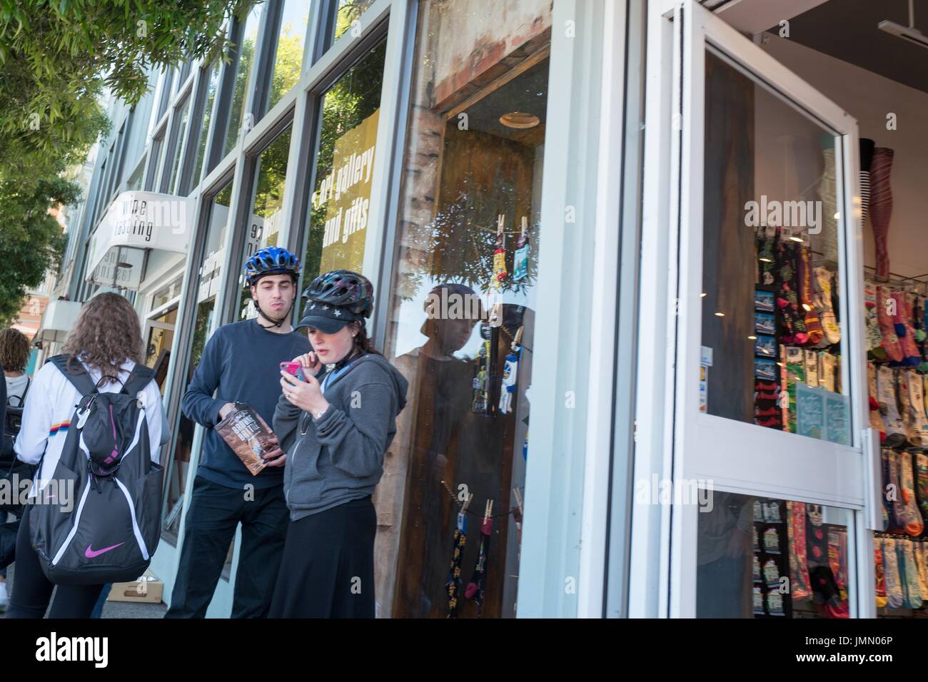 Two Millennial age cyclists wearing helmets stand outside a store on Bridgeway road in downtown Sausalito, California, June 29, 2017. Stock Photo
