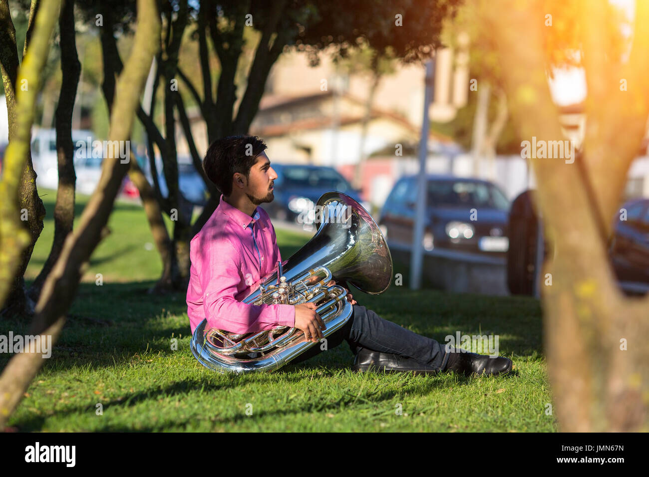 Musician instrumentalist with the tuba sitting on the grass in the Park. Stock Photo