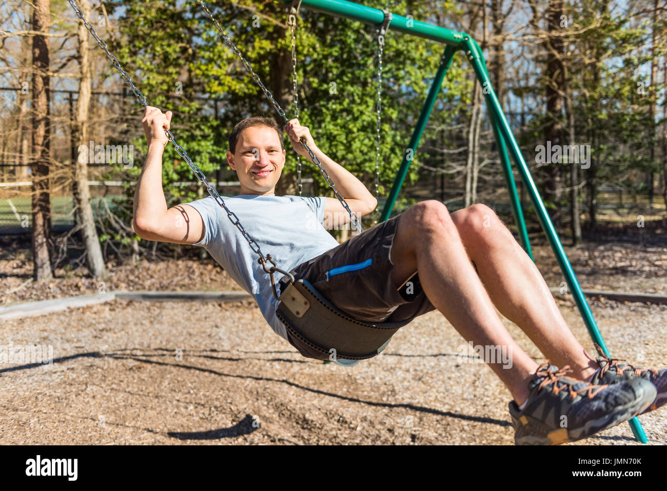 Young happy man on swing in playground smiling Stock Photo Alamy