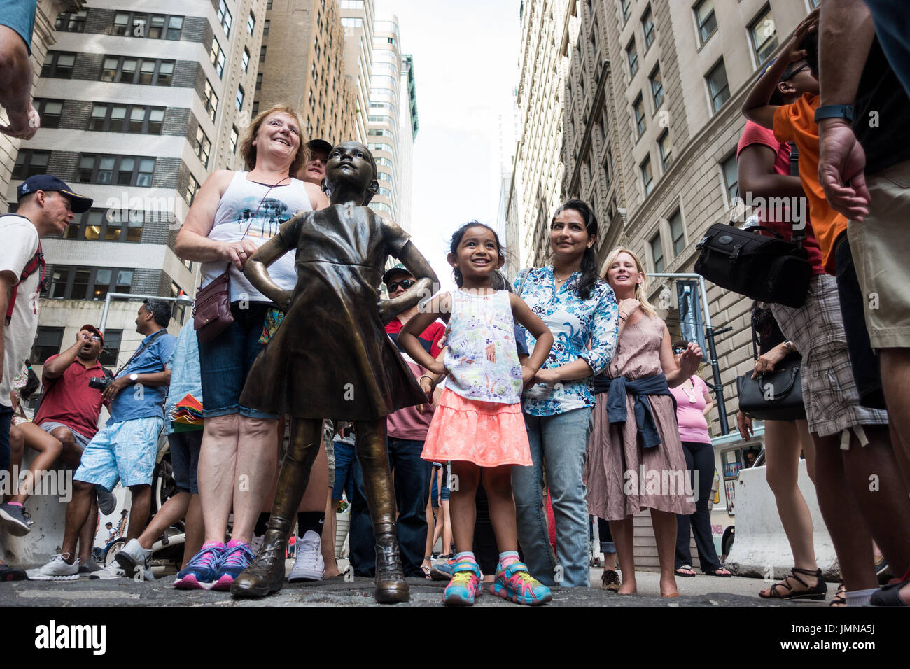 Young girl, with her family, posing at the front of the Fearless Girl bronze sculpture on Wall Street, NY Stock Photo