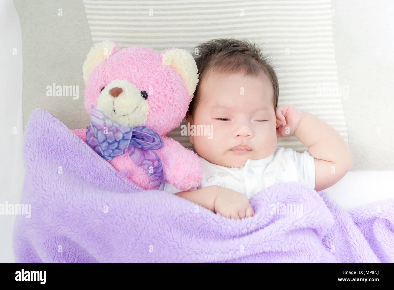 Portrait of adorable baby girl sleeping on the bed with bear doll Stock