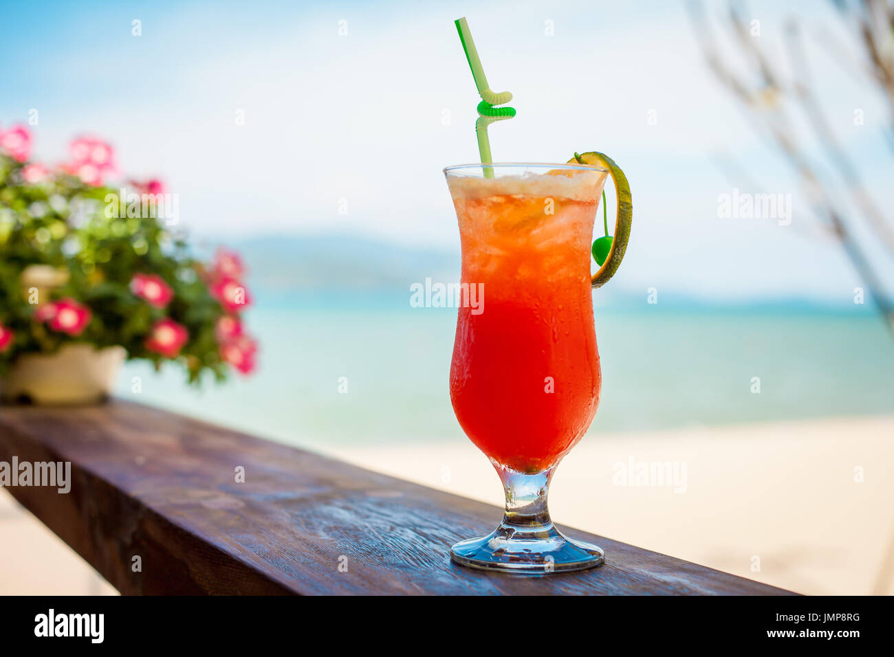 Close up of glass with refreshing orange cocktail with cherry on table on beach. Stock Photo