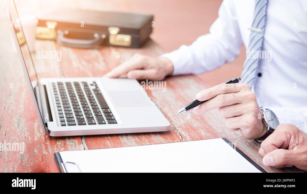 Two businessmen discussing planing tasks with laptop computer sitting at outdoor table. Stock Photo