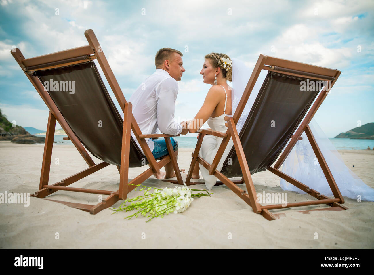 Bride and groom sitting in lounge chair by the sea on their wedding day ...